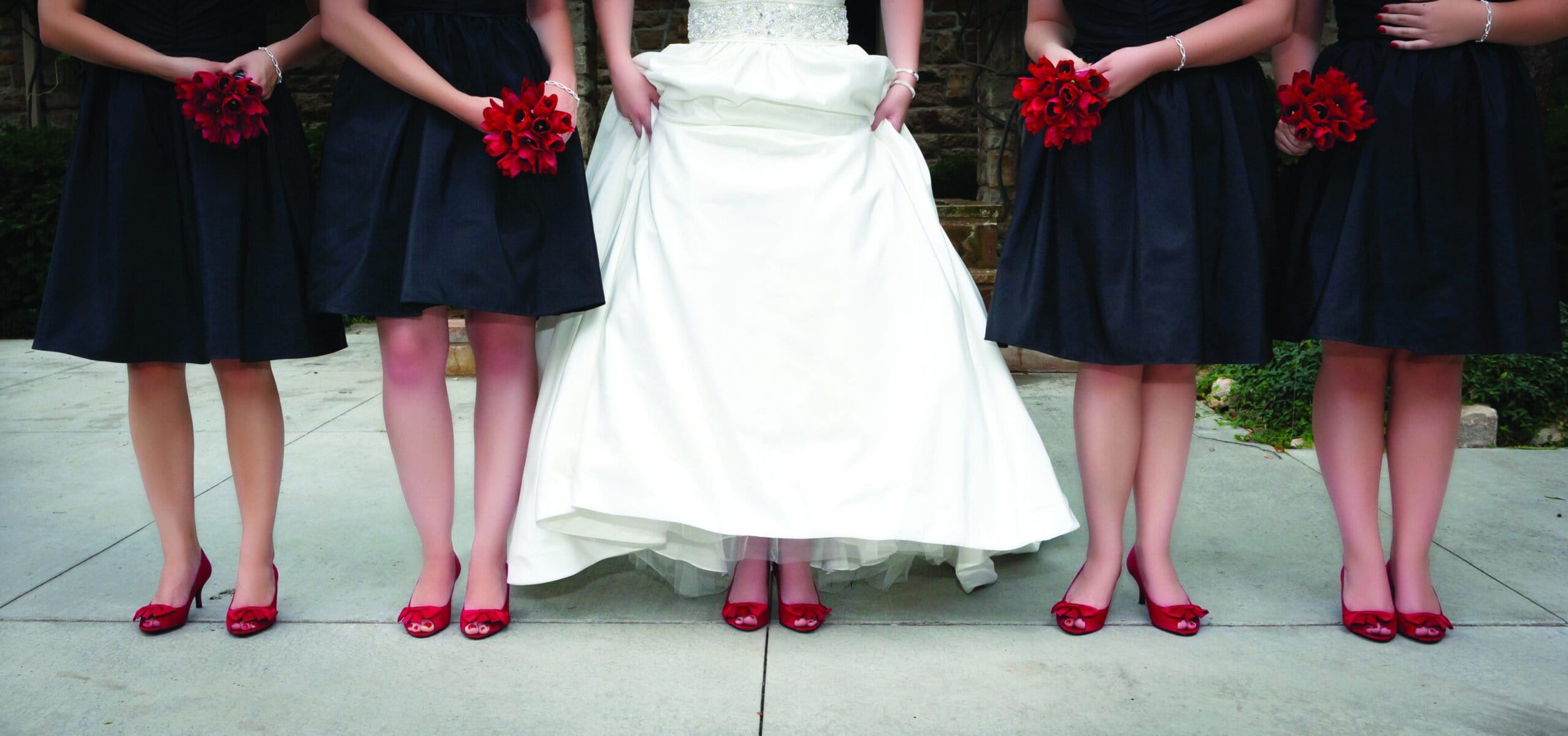 Bridesmaids and bride wearing red shoes and holding red bouquets.