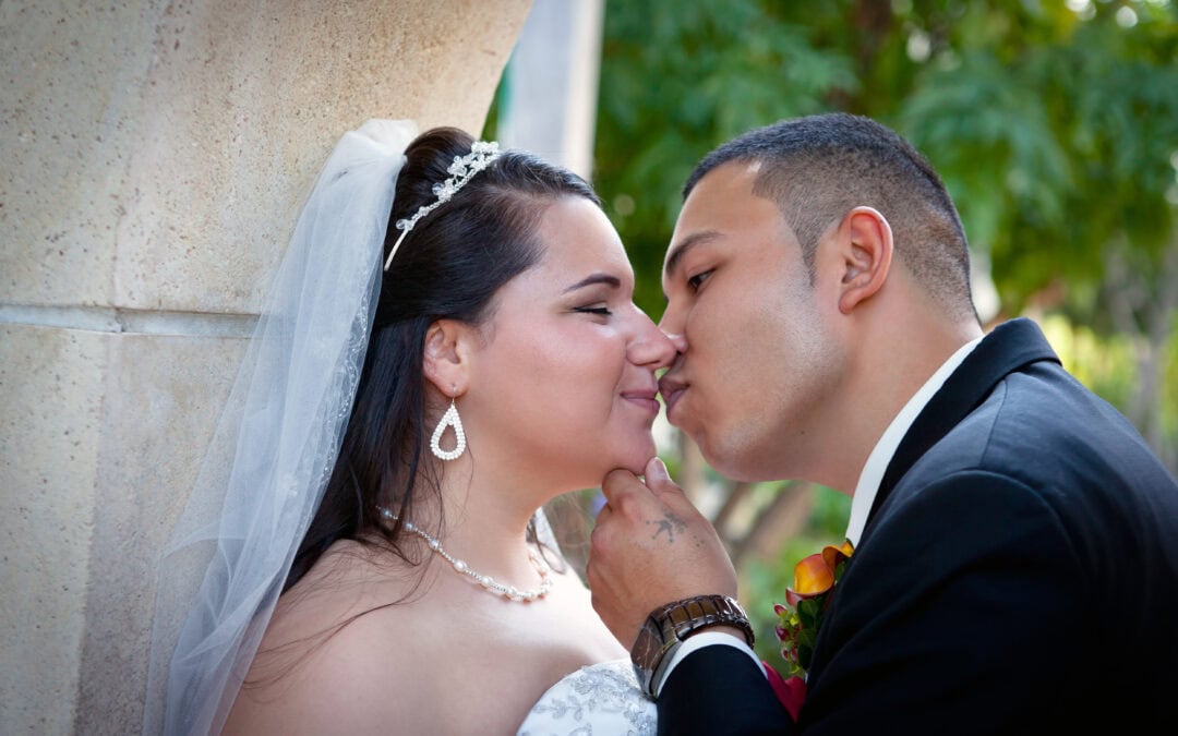 Bride and groom sharing a romantic kiss outdoors on wedding day.