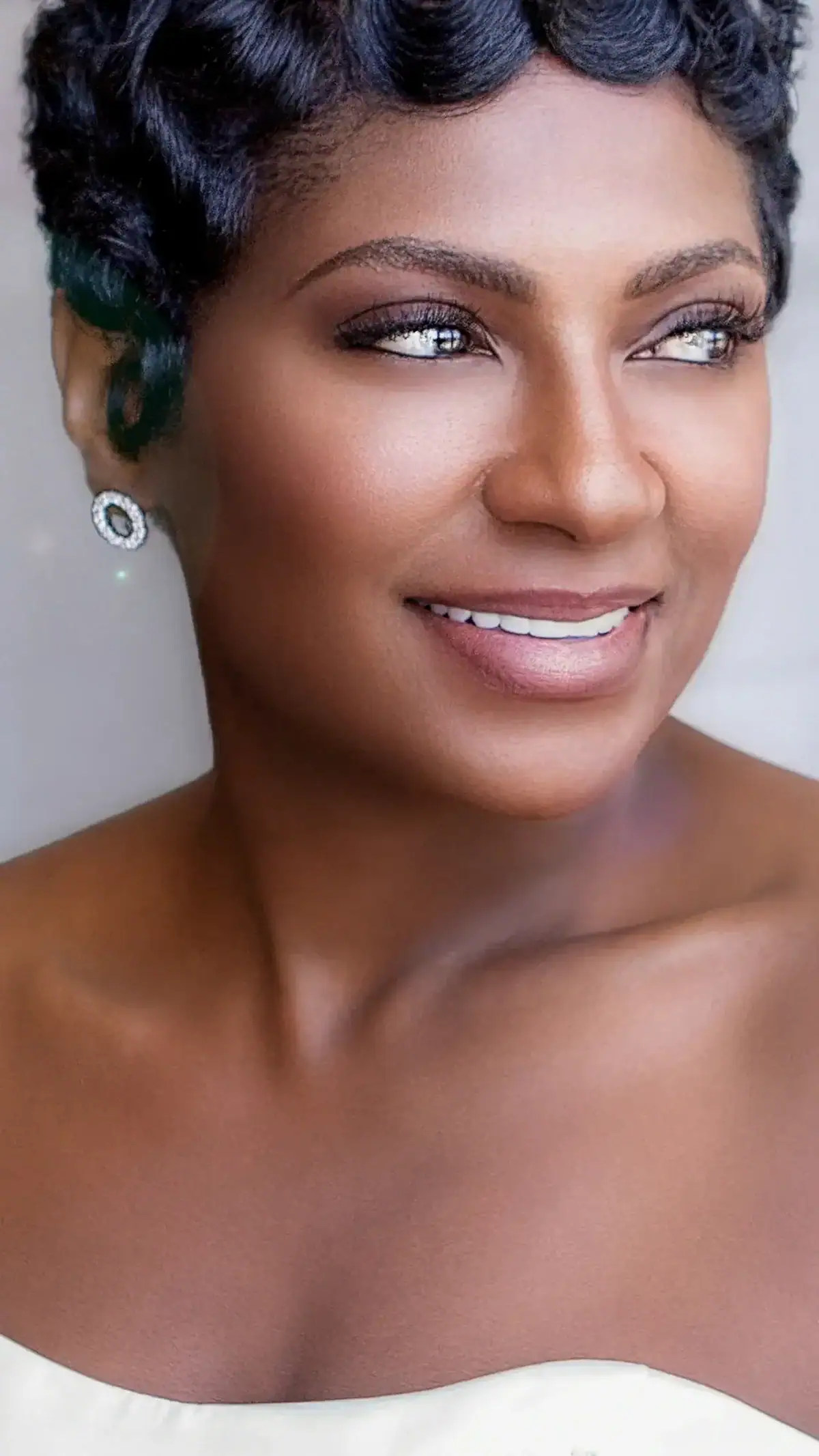 Close-up of a smiling woman with short curly hair and earrings.