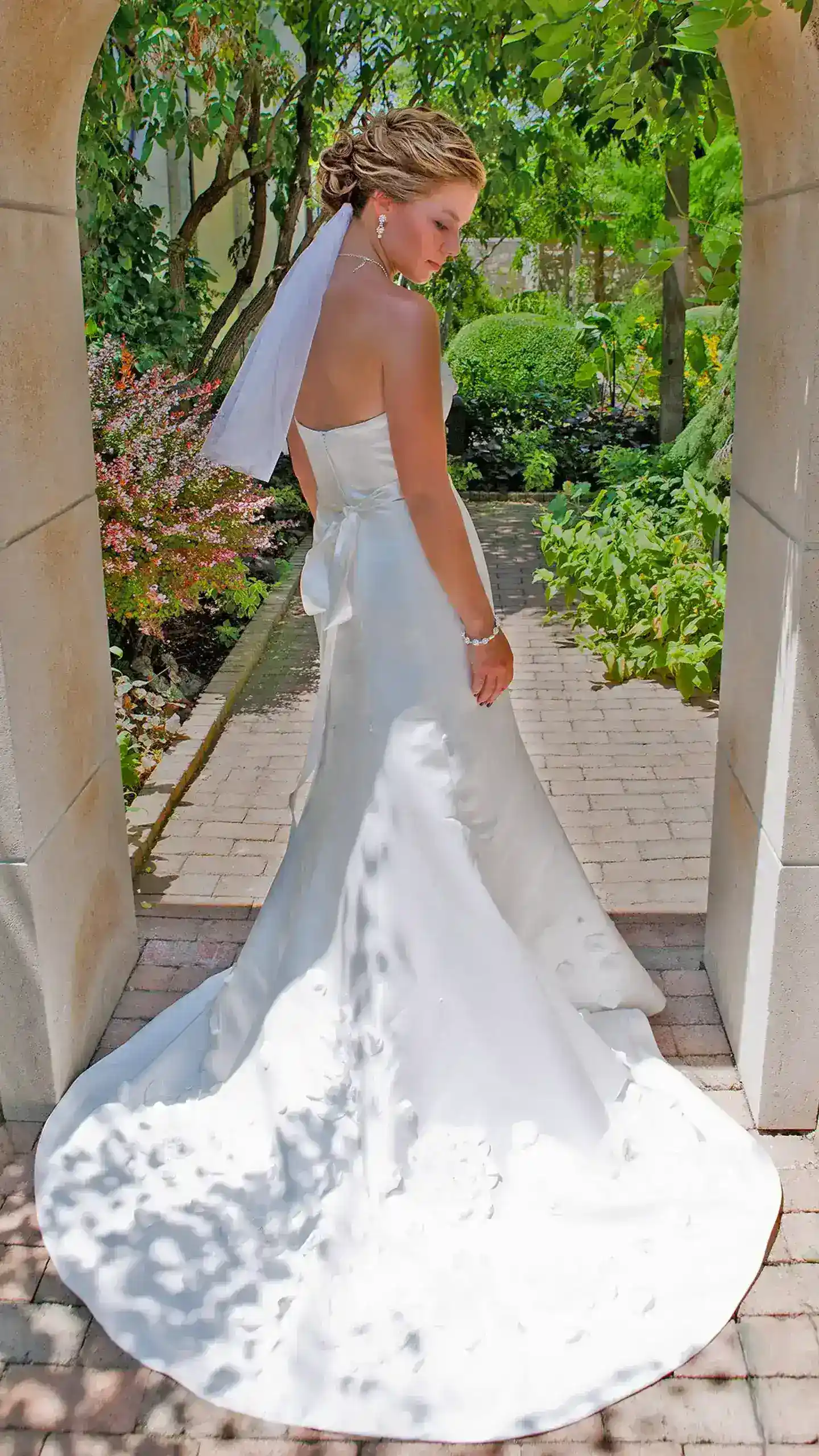 Bride in white wedding gown standing in garden archway.