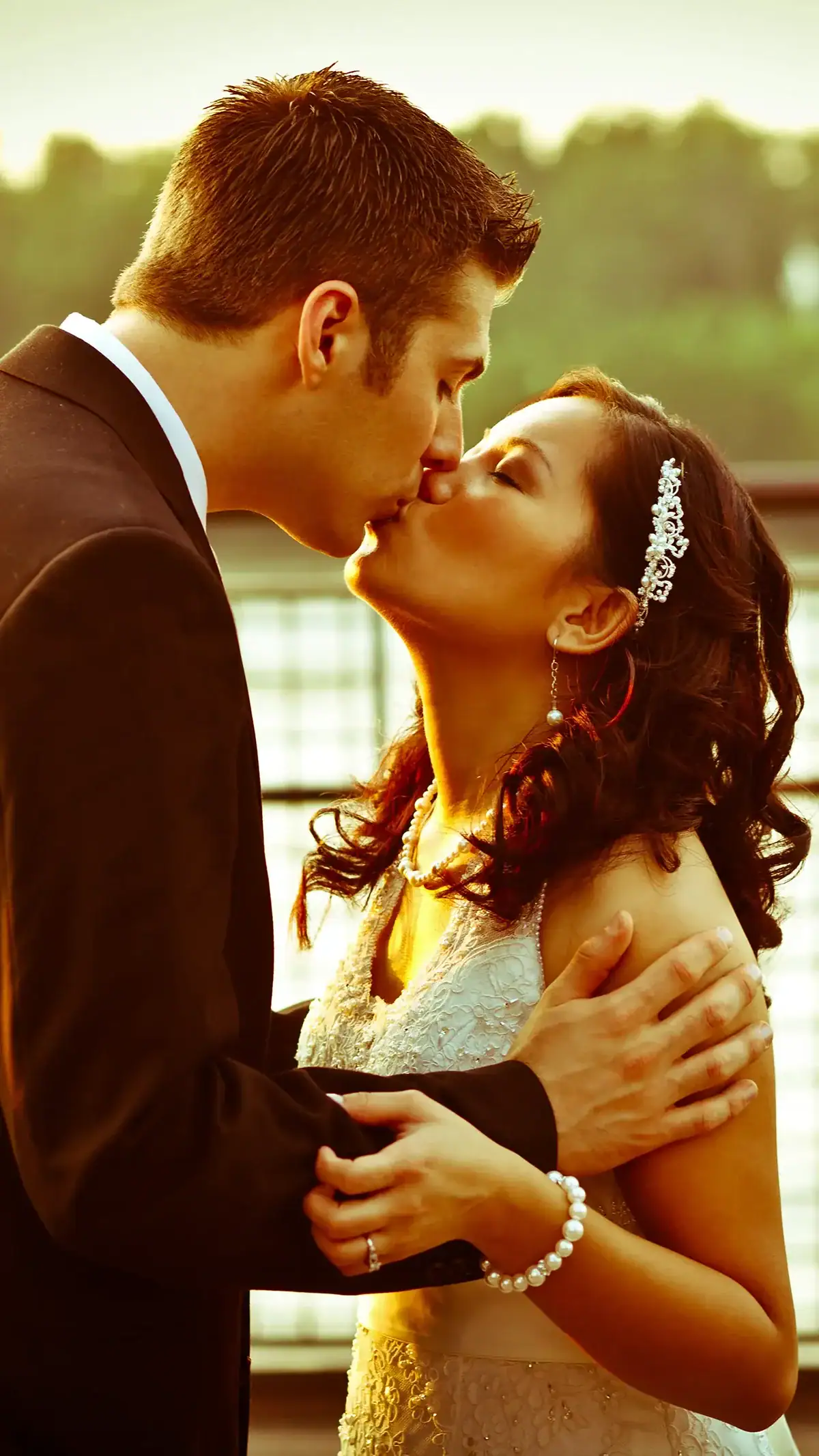 Romantic wedding couple sharing a kiss outdoors at sunset.